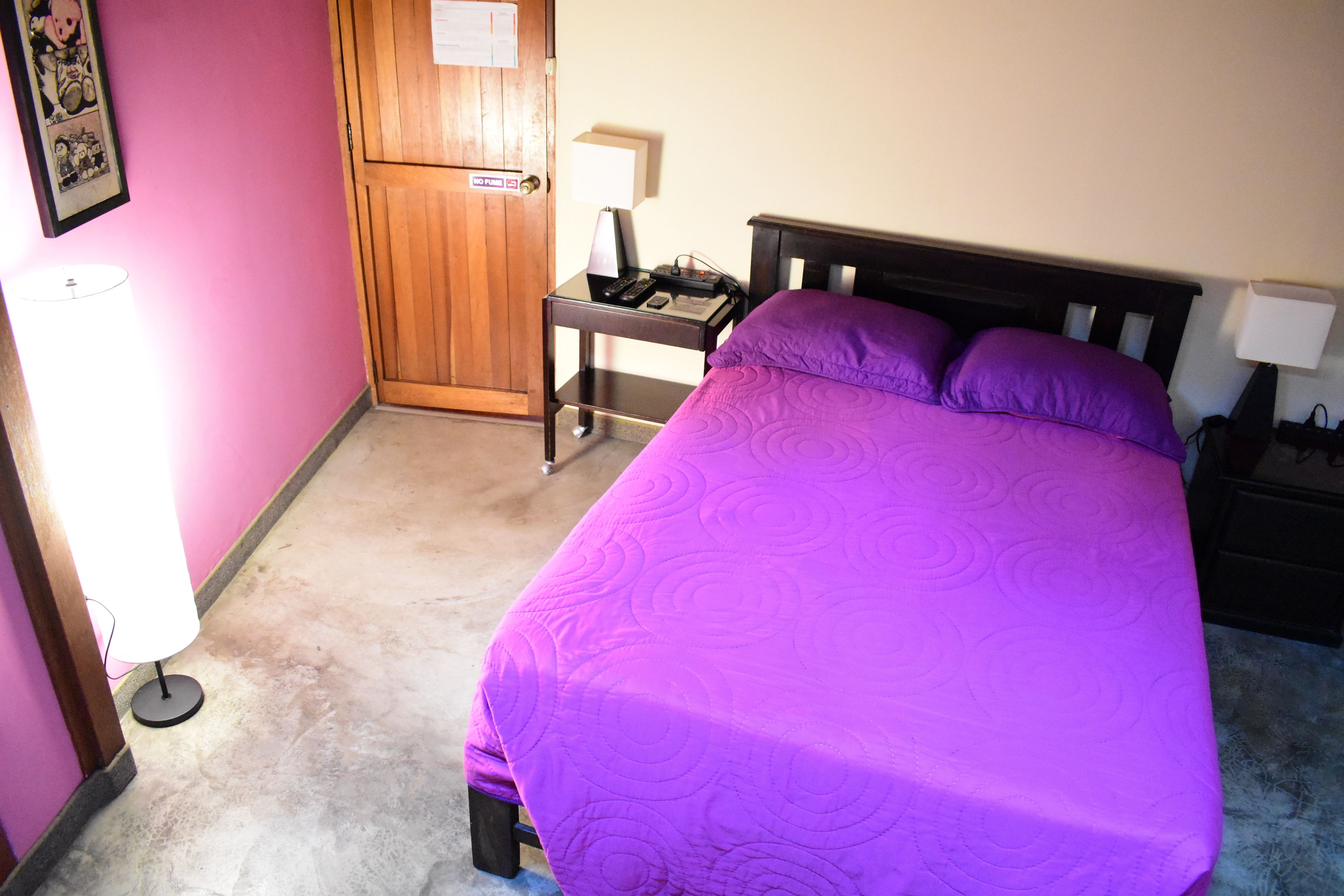 Una habitación con cama, mesita de noche, escritorio, lámpara y puerta.