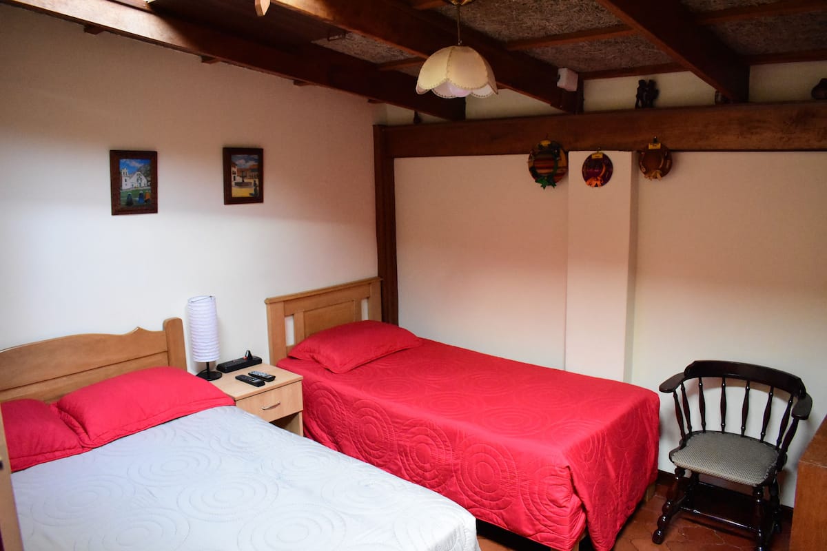A bedroom with two beds, a chair, and a nightstand with a lamp.
