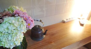 A wooden countertop with a tea kettle, a power strip, and a remote control.