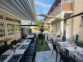 Un espacio de comedor al aire libre con mesas y sillas, un pérgola y vistas a la calle.