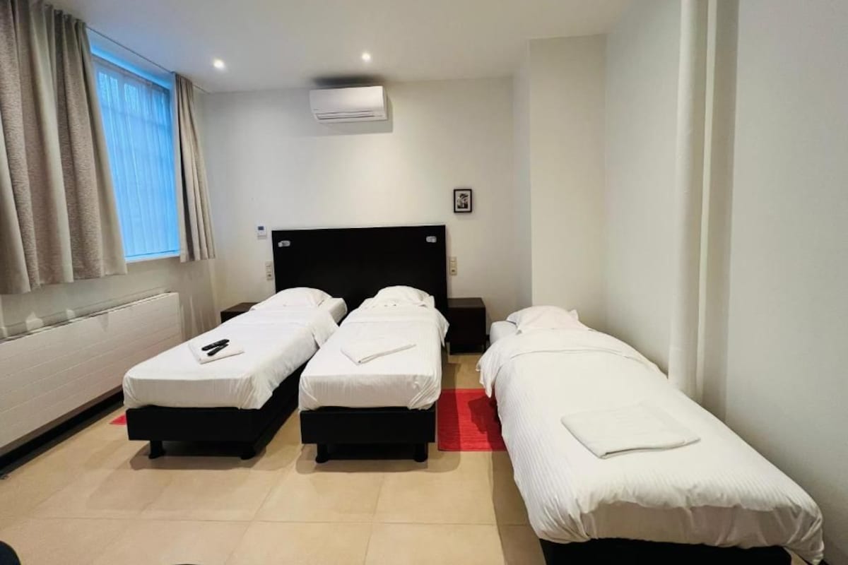 A hotel room with three single beds, a red rug, and an air conditioning unit on the wall.