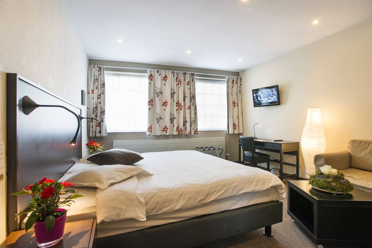 Ein Hotelzimmer mit Bett, Nachttisch, Fernseher, Schreibtisch und Blick ins Freie.