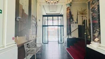 Un hall d’hôtel avec un lustre, un banc, une moquette rouge et un escalier.