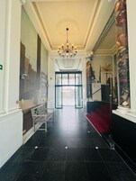 En hotelllobby med en kristallkrona, en bänk, en röd matta och en trappa.