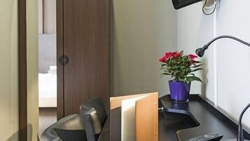 Una habitación de hotel con un escritorio, una silla, un televisor montado en la pared, una planta en maceta y un armario.