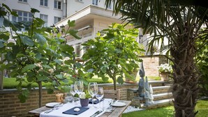 Un área de comedor al aire libre con una mesa dispuesta para dos personas, rodeada de follaje y una palmera.