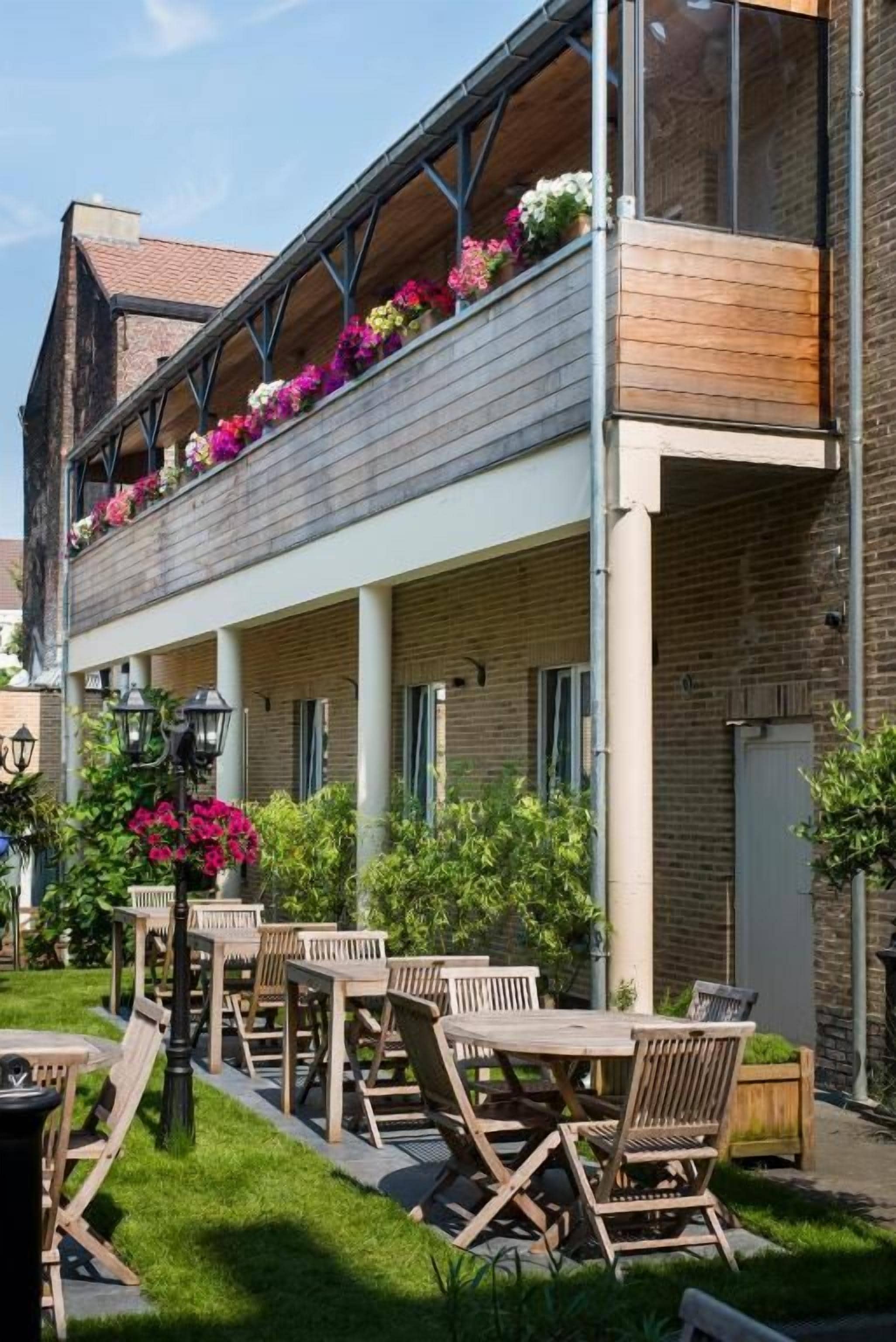 Un bâtiment doté d’un balcon en bois, d’un espace extérieur aménagé pour s’asseoir et d’une façade en briques.