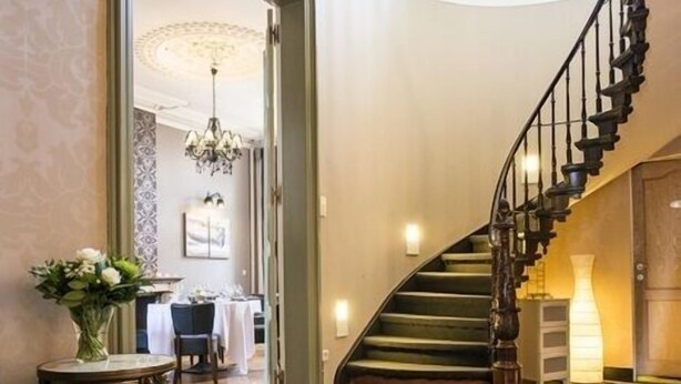 Una gran escalera de diseño curvo que conduce a un comedor con una araña y una mesa puesta para comer.