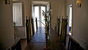 A long, wooden dining table with a vase of flowers in the center, flanked by wall sconces and a view of a door and window. - Oasis Backpackers' Mansion Lisboa (Lisbon)