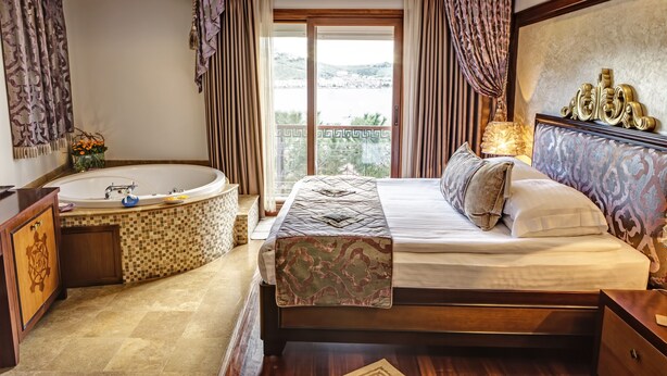 A bedroom with a large bed, a bathtub, and a balcony with a view. - Bülbül Yuvasi Boutique Hotel - Boutique Class (Foça)