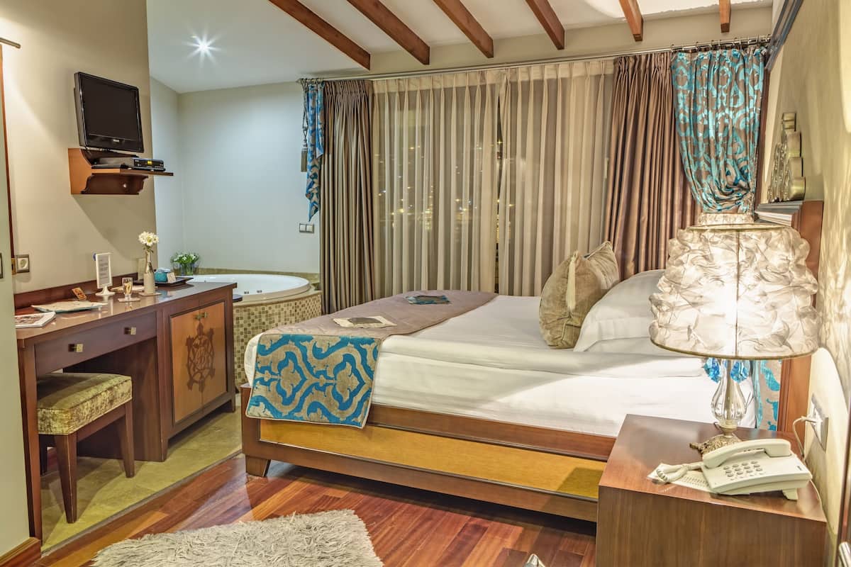 A bedroom with a bed, bedside table, lamp, and a desk with a chair.