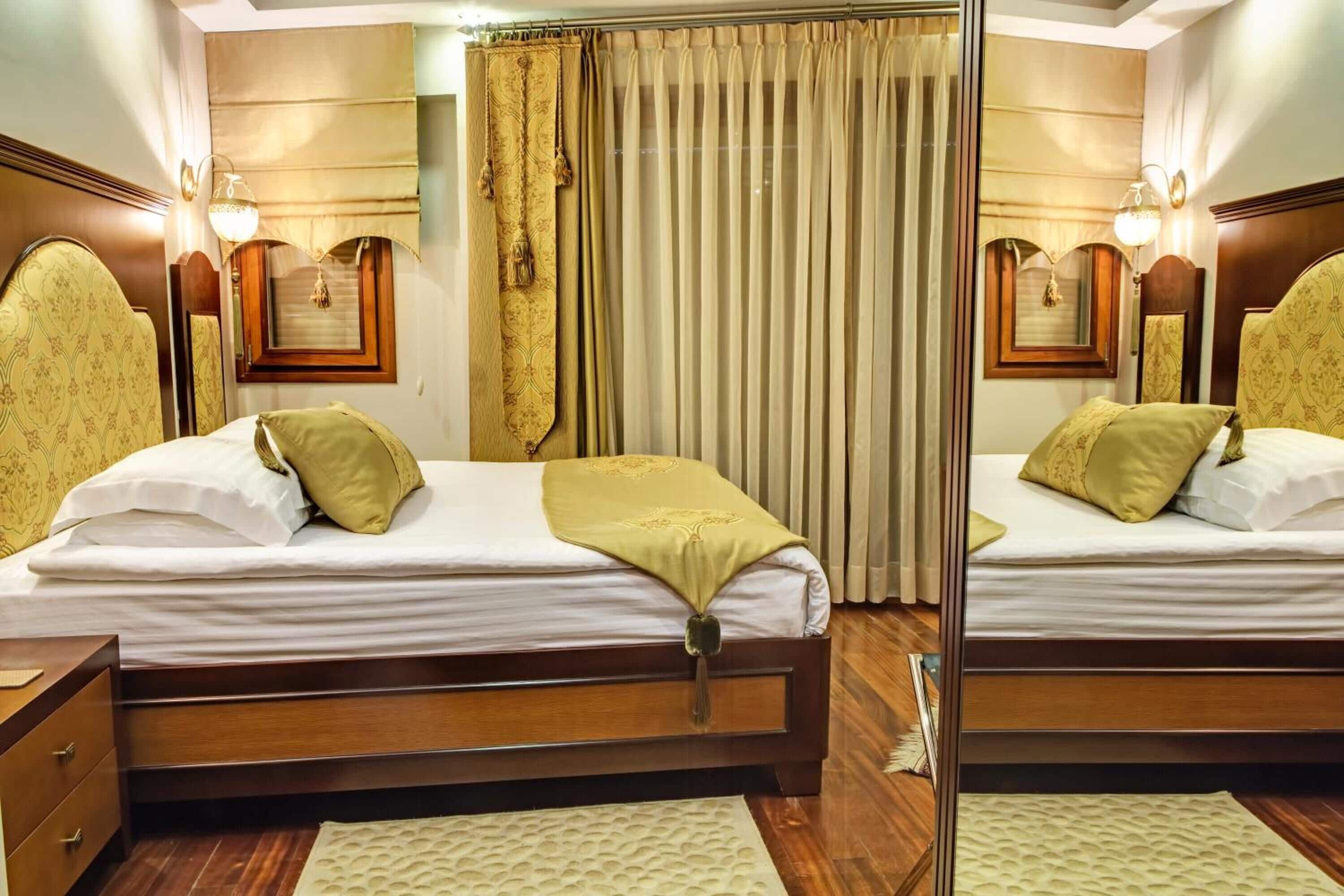 Habitación de hotel con espejos, dos camas y cabeceros de madera.