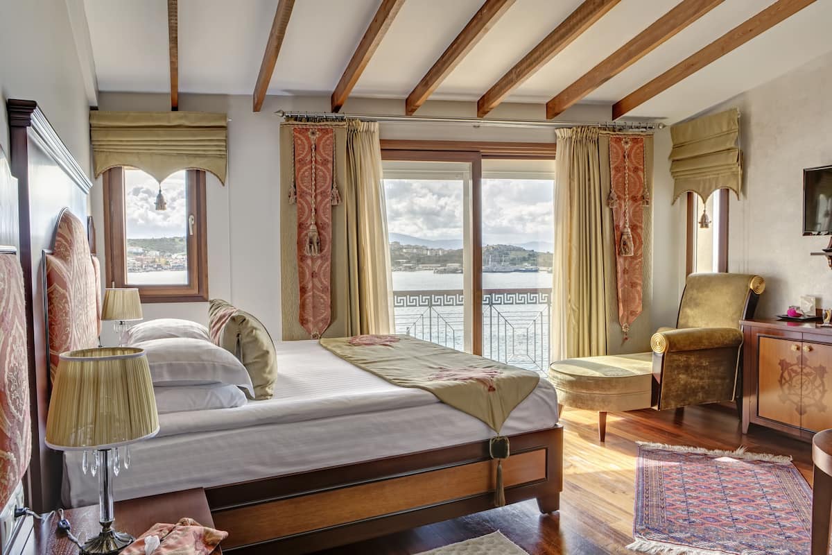 A bedroom with a bed, a chair, a desk, and a view of the sea.