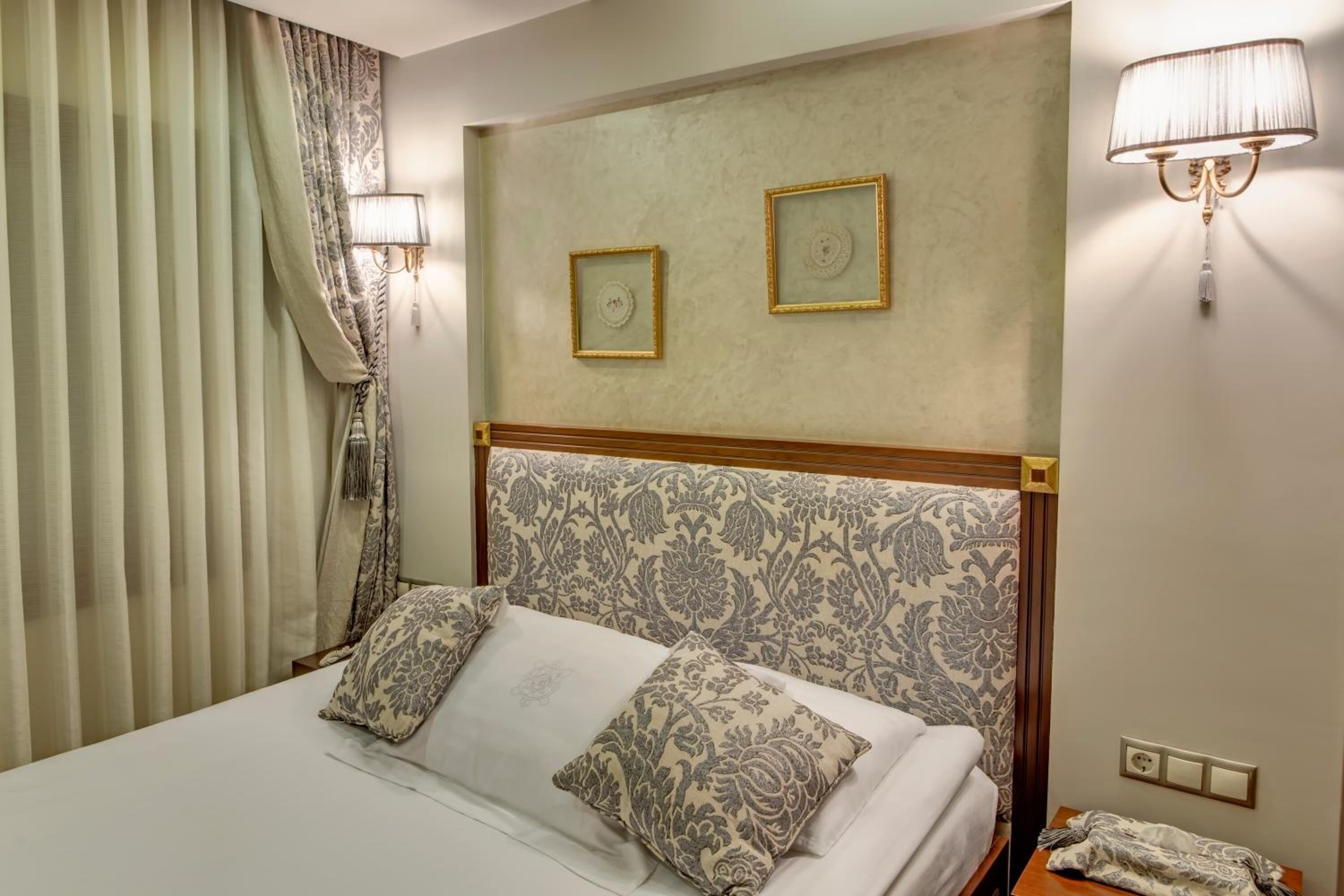 A hotel room with a bed, two wall-mounted lamps, and two framed pictures on the wall.