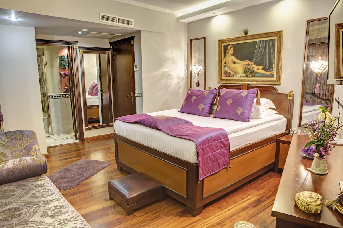 A well-appointed bedroom with a large bed, a sitting area with a sofa, and a vanity with a mirror.