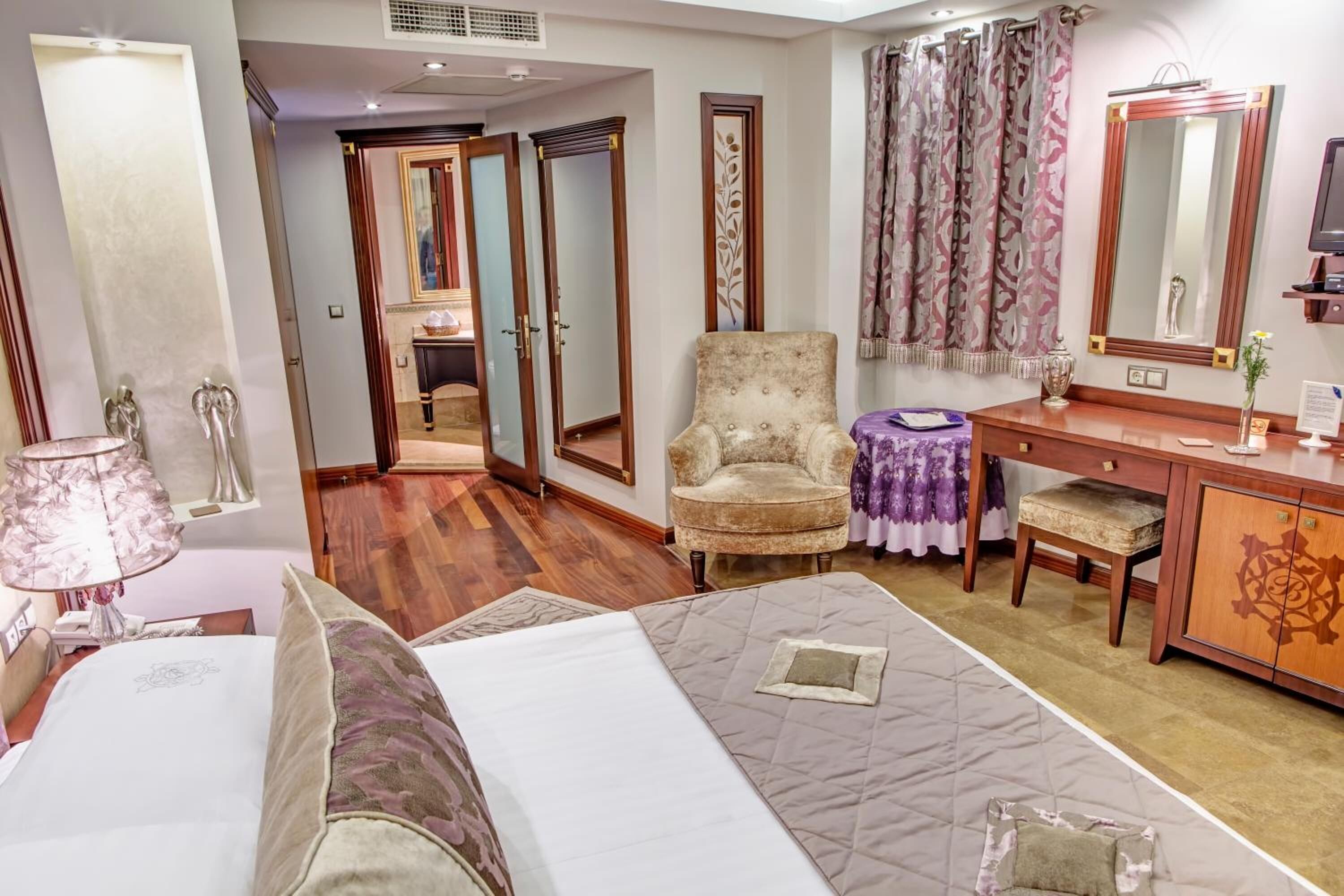 A hotel room with a bed, a chair, a desk, a mirror, and a wardrobe.