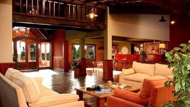 A spacious lobby with a high ceiling, a wooden staircase, and a seating area with a coffee table. - Hostería Posta Sur (El Calafate)