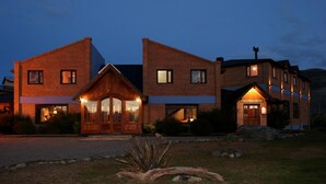 A two-story brick building with a restaurant sign, large windows, and a well-maintained lawn. - Hostería Posta Sur (El Calafate)