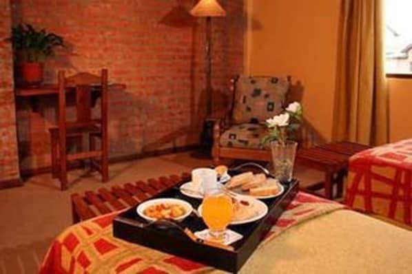 Habitación de hotel con una bandeja de desayuno sobre la cama, una silla, una mesa y una lámpara.
