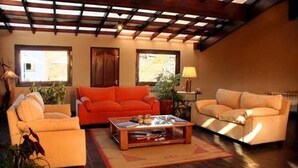 A living room with a wooden ceiling, two sofas, a coffee table, and a lamp. - Hostería Posta Sur (El Calafate)