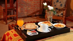 A breakfast tray with bread, juice, and a cup on a table in a room with a brick wall and a patterned chair. - Hostería Posta Sur (El Calafate)
