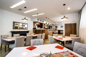 A dining area with tables set for two, a bar area with a clock, and a mirror on the wall. - Grand Hotel Trencin (Trencin)