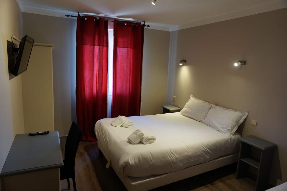 Ein Hotelzimmer mit Bett, Schreibtisch, Stuhl, einem an der Wand montierten Fernseher und einem roten Vorhang.
