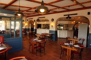 A restaurant interior with wooden tables and chairs, a kitchen area, and a bar. - Hôtel Le Bistrot D'orange (Orange)
