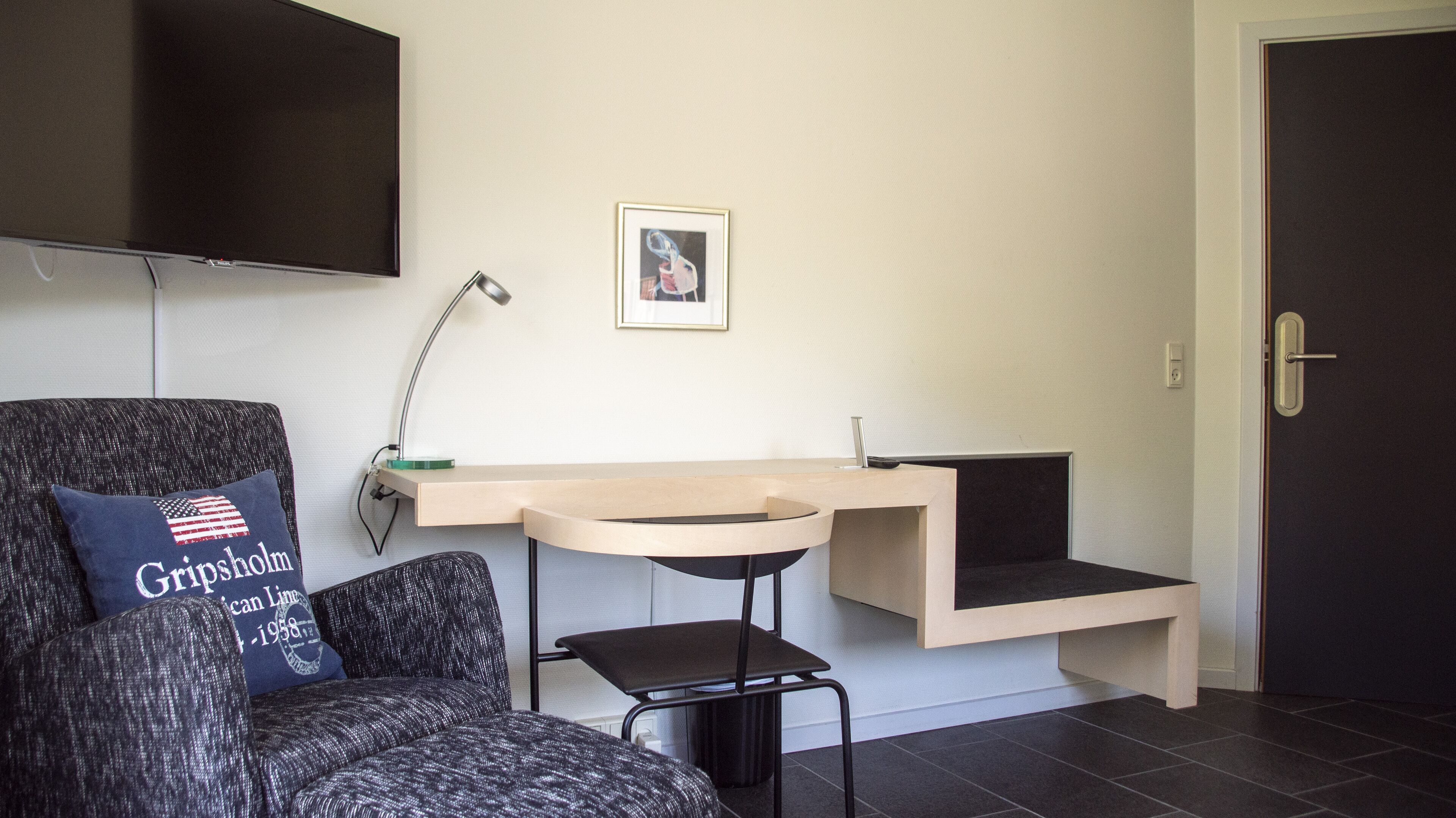A modern room with a desk, chair, and a TV mounted on the wall.