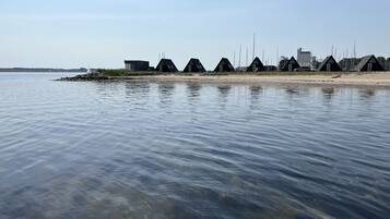 A row of beachside cottages with a clear view of the water and distant city skyline.