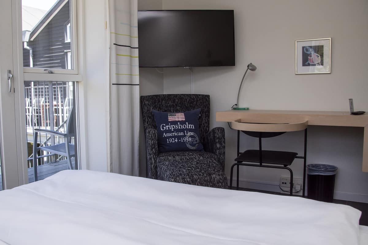 A hotel room with a bed, a chair with an American flag pillow, a desk, and a TV on the wall.
