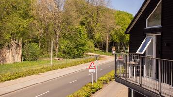 A road with a bicycle crossing sign, a wooden house with a balcony, and a forested hillside.