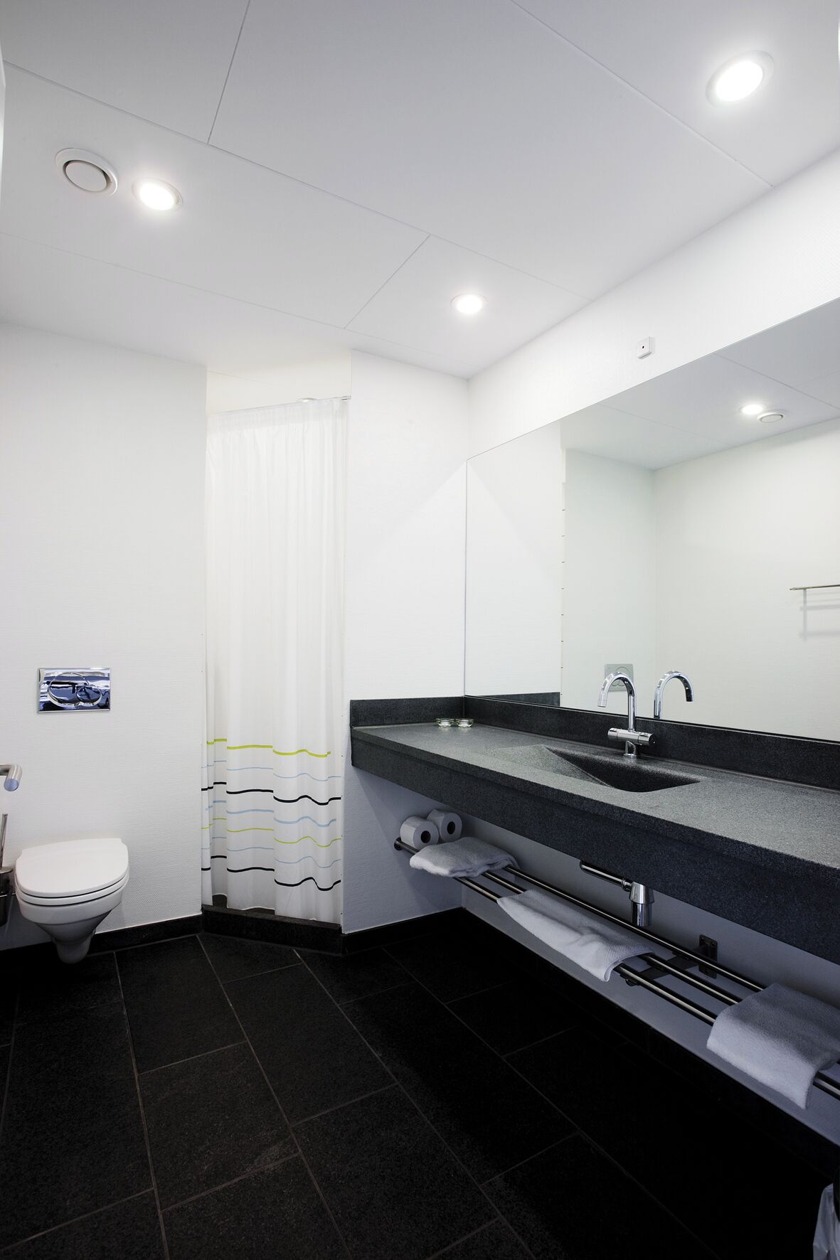 A modern bathroom with a white toilet, a black sink with a mirror, and a shower curtain with wavy patterns.