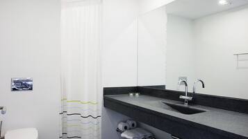 A modern bathroom with a white toilet, a black sink with a mirror, and a shower curtain with wavy patterns.