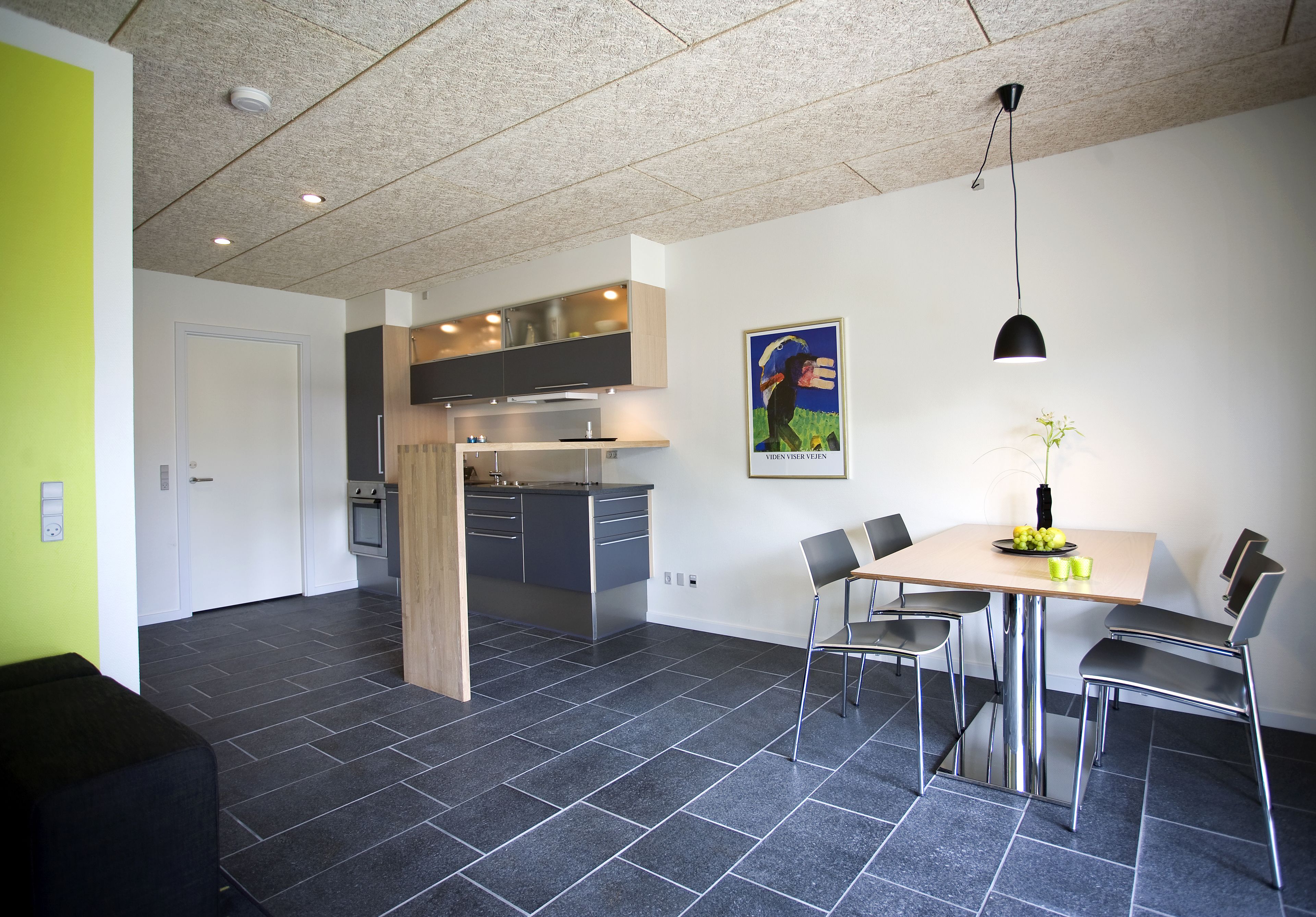 A modern kitchen with grey cabinets, a stainless steel range hood, and a dining area with a table and chairs.