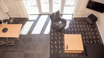 Una habitación moderna con una mesa de madera, una alfombra estampada, una silla y un televisor montado en la pared.