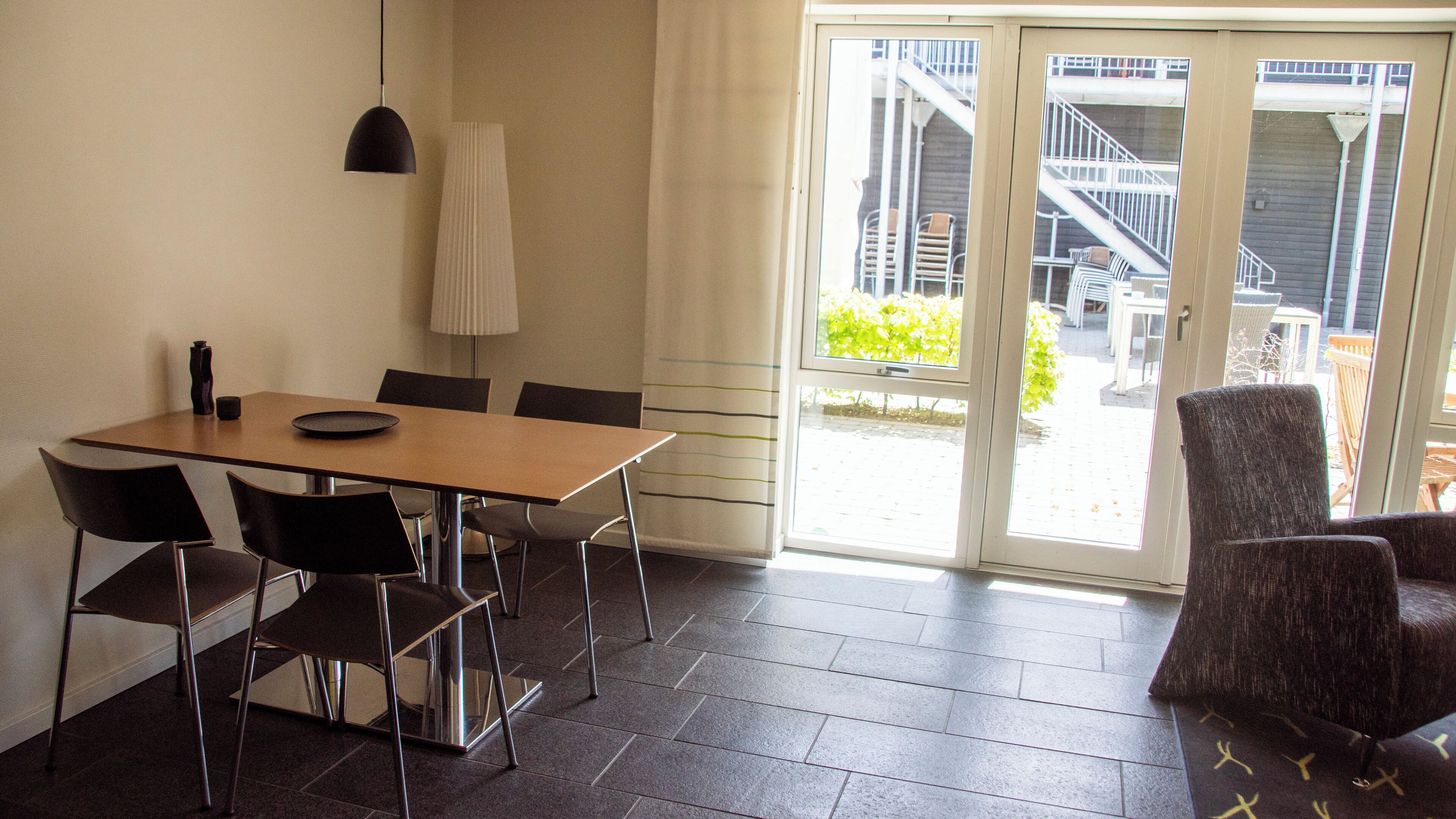 A dining area with a table and chairs, a lamp, and a view of the outside through a glass door.