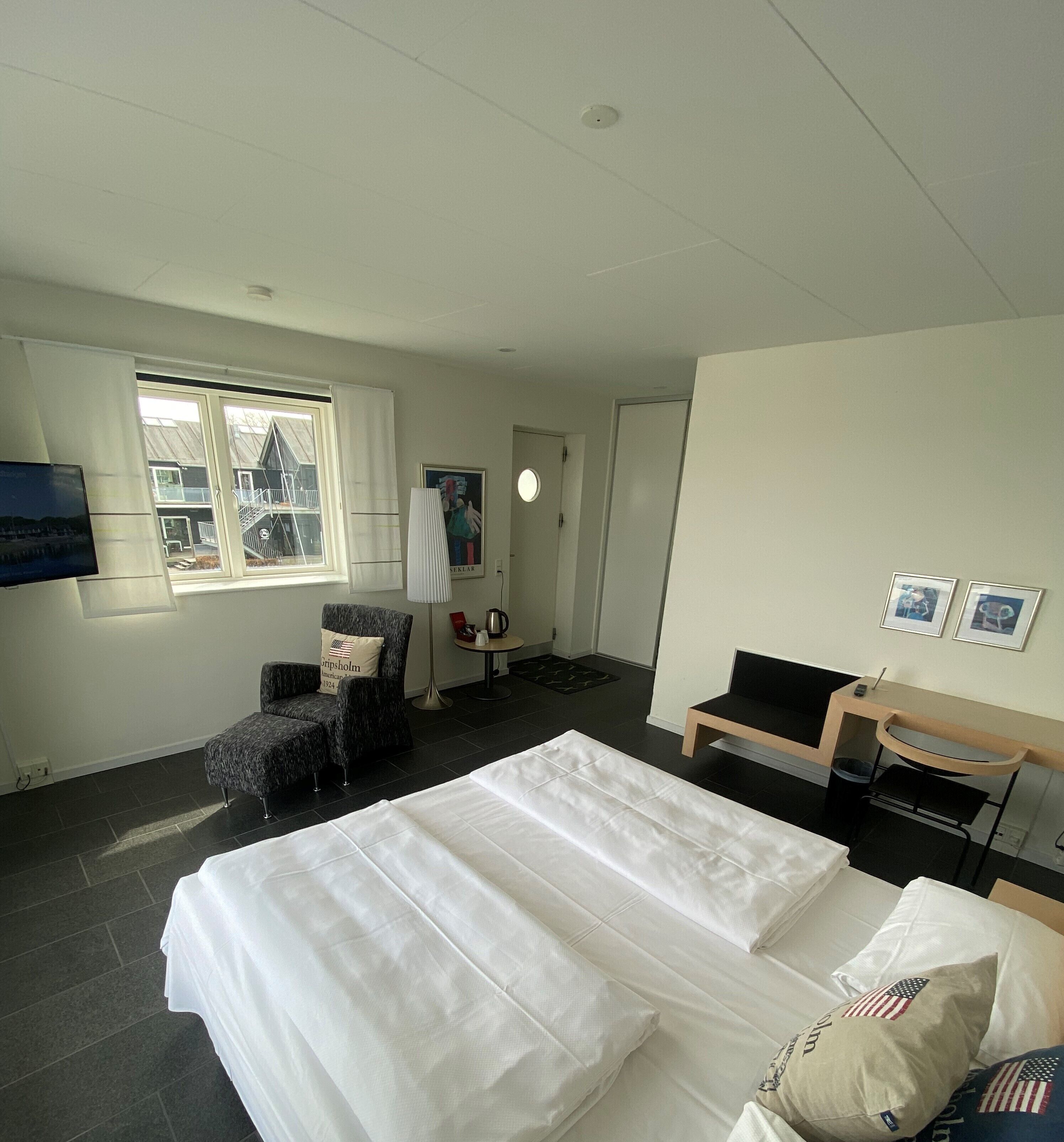 A hotel room with a bed, a chair, a desk, a window with a view, and a poster on the wall.