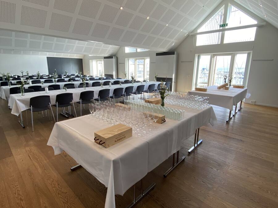 Ein geräumiger Konferenzraum mit hohen Decken und großen Fenstern, ausgestattet mit Tischen für eine Besprechung oder Veranstaltung.