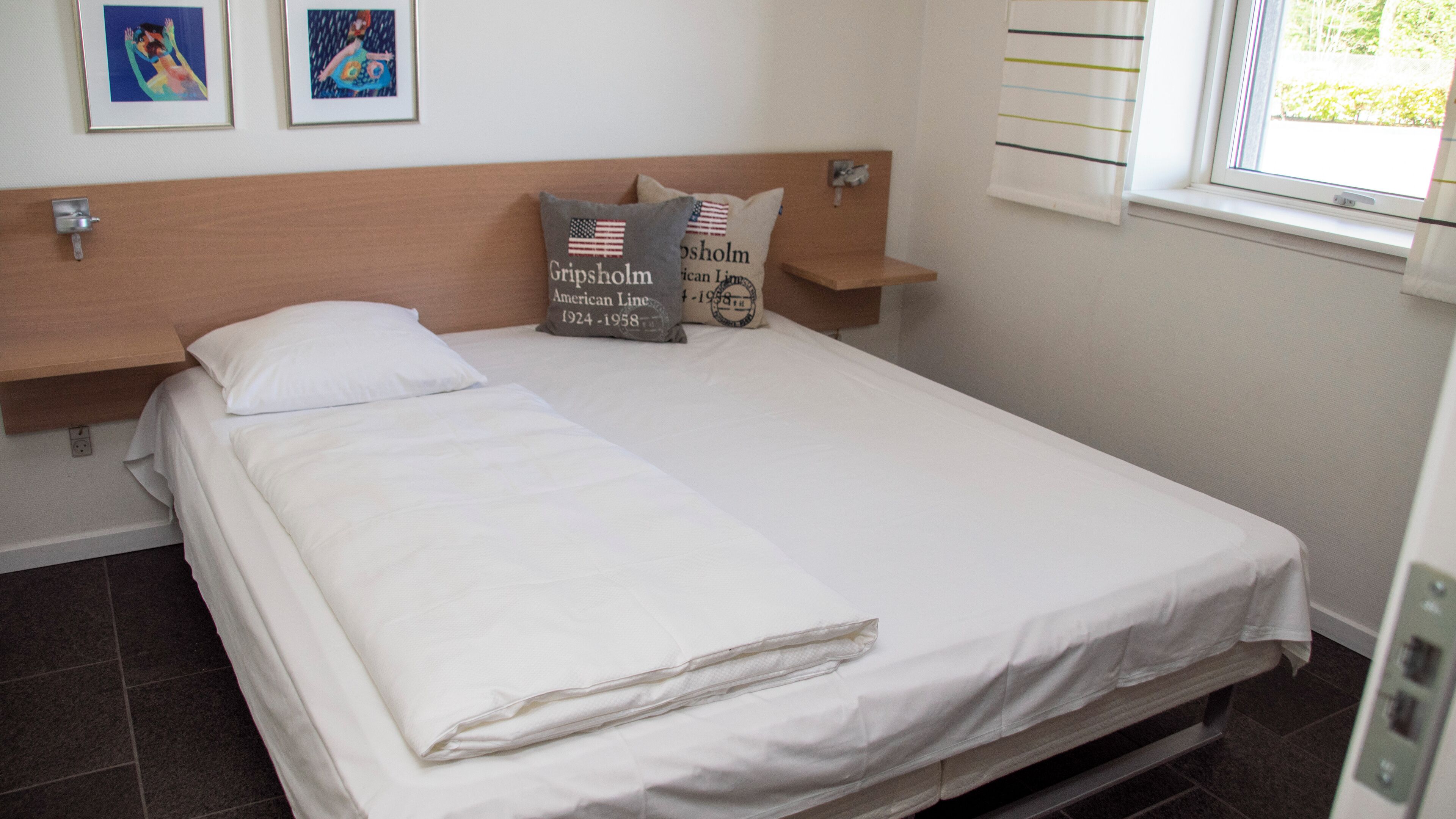 A neatly made bed with white linens, a wooden headboard, and two pillows with American flags and text.