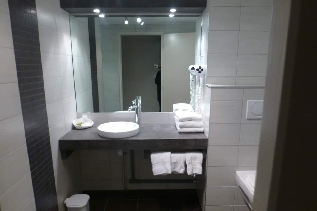 A modern bathroom with a round sink, a mirror, a towel rack, and a toilet.