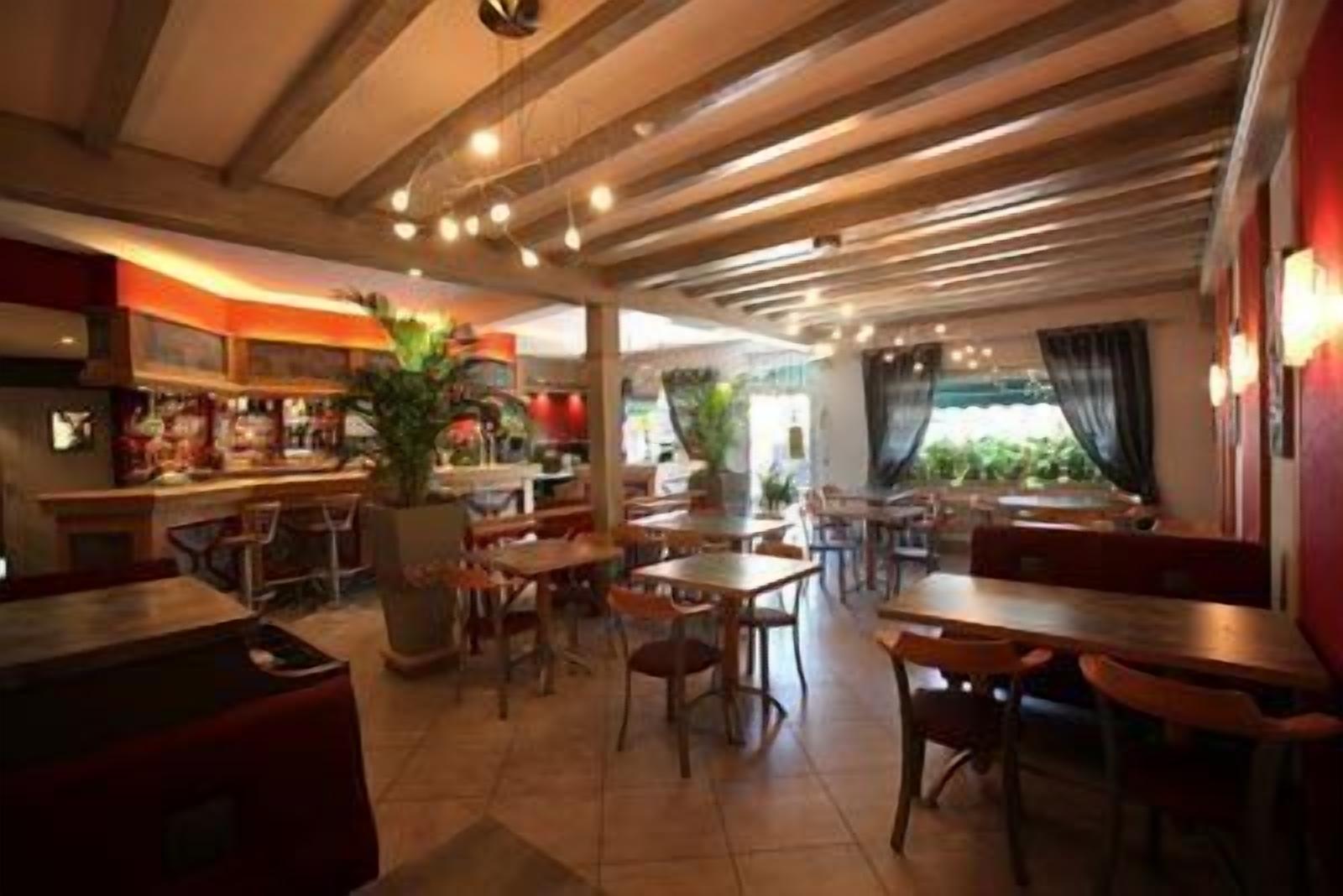 A restaurant with wooden ceiling beams, tables, chairs, and a bar area.