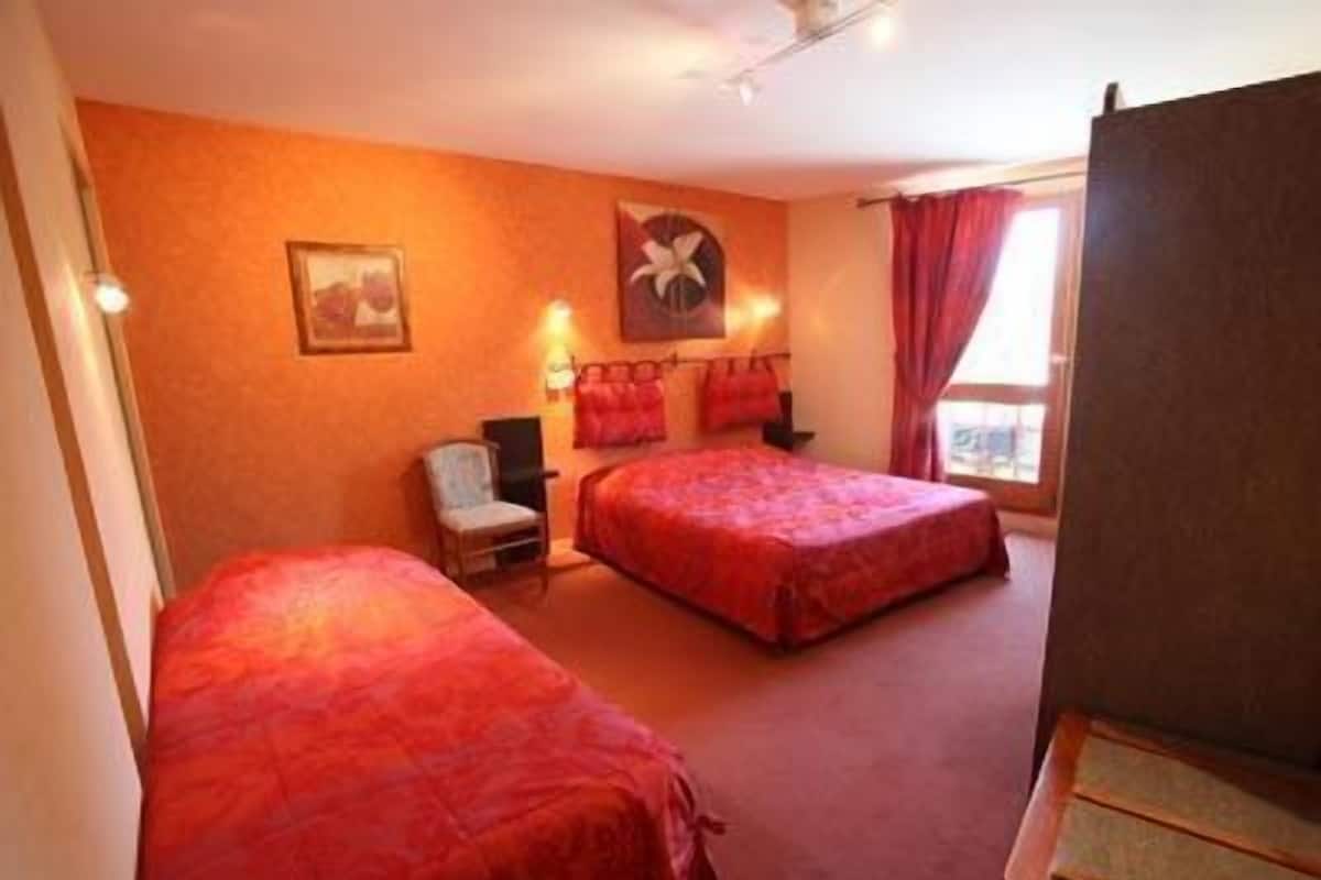 A hotel room with two beds, a chair, a desk, and a window with curtains.