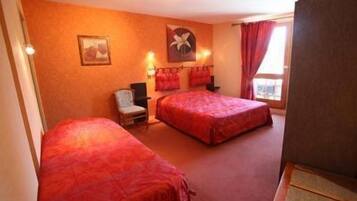 A hotel room with two beds, a chair, a desk, and a window with curtains.