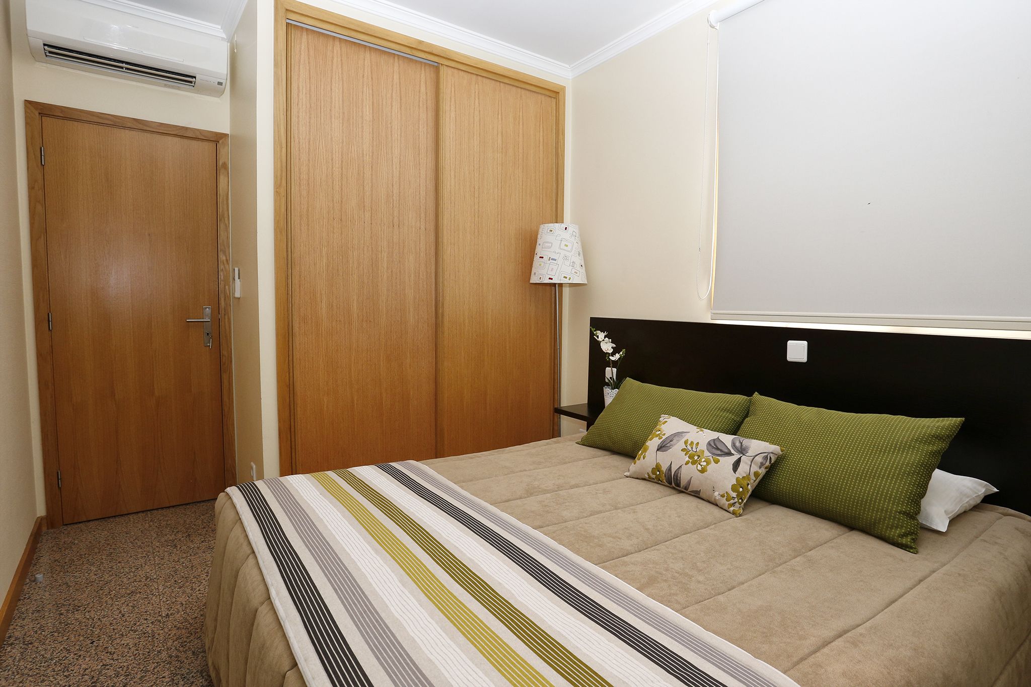 Une chambre à coucher comprenant un lit, une armoire, une lampe et un climatiseur fixé au mur.