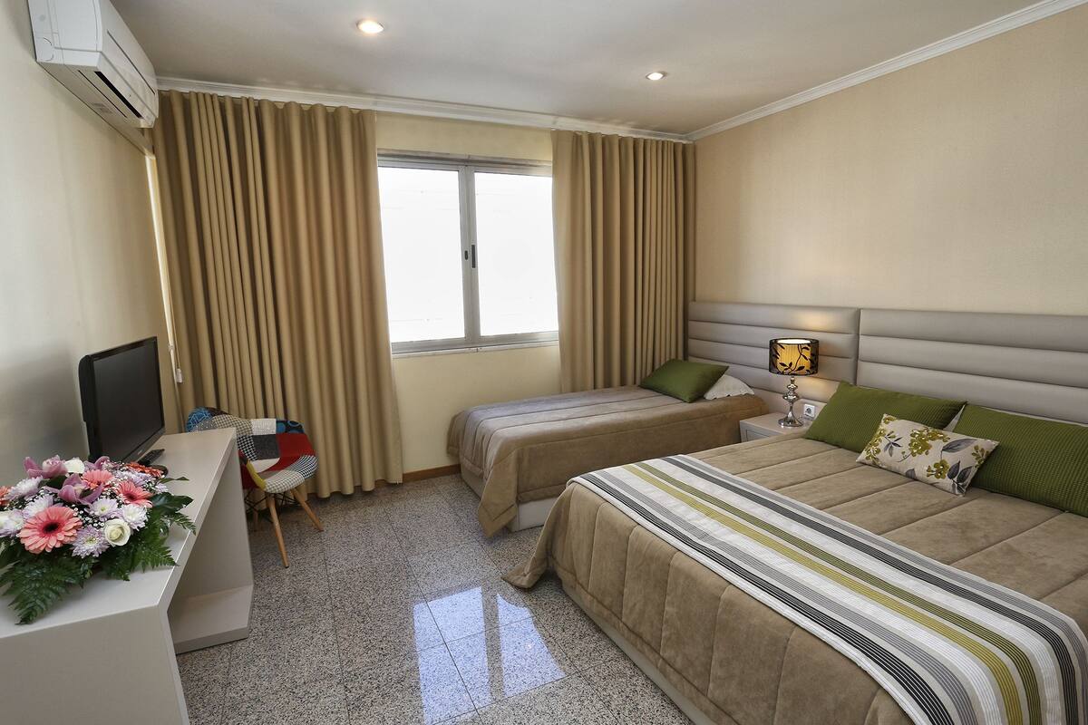 Une chambre d’hôtel avec deux lits, un bureau avec une télévision et une fenêtre avec des rideaux.