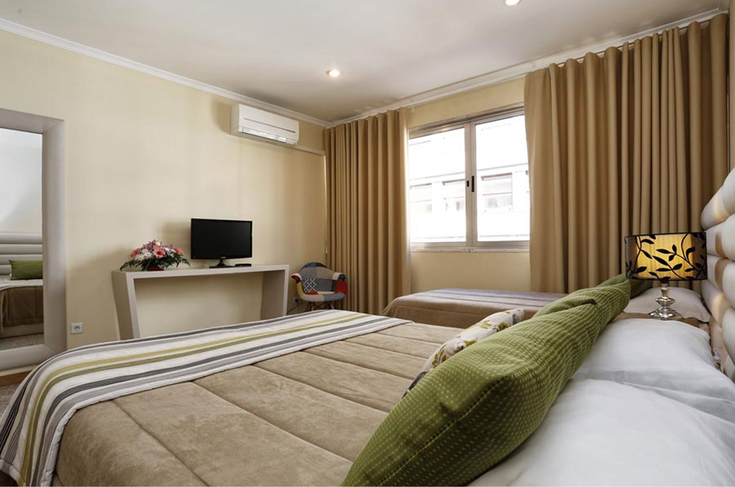 A hotel room with a bed, a desk with a TV, a chair, and a window with curtains.
