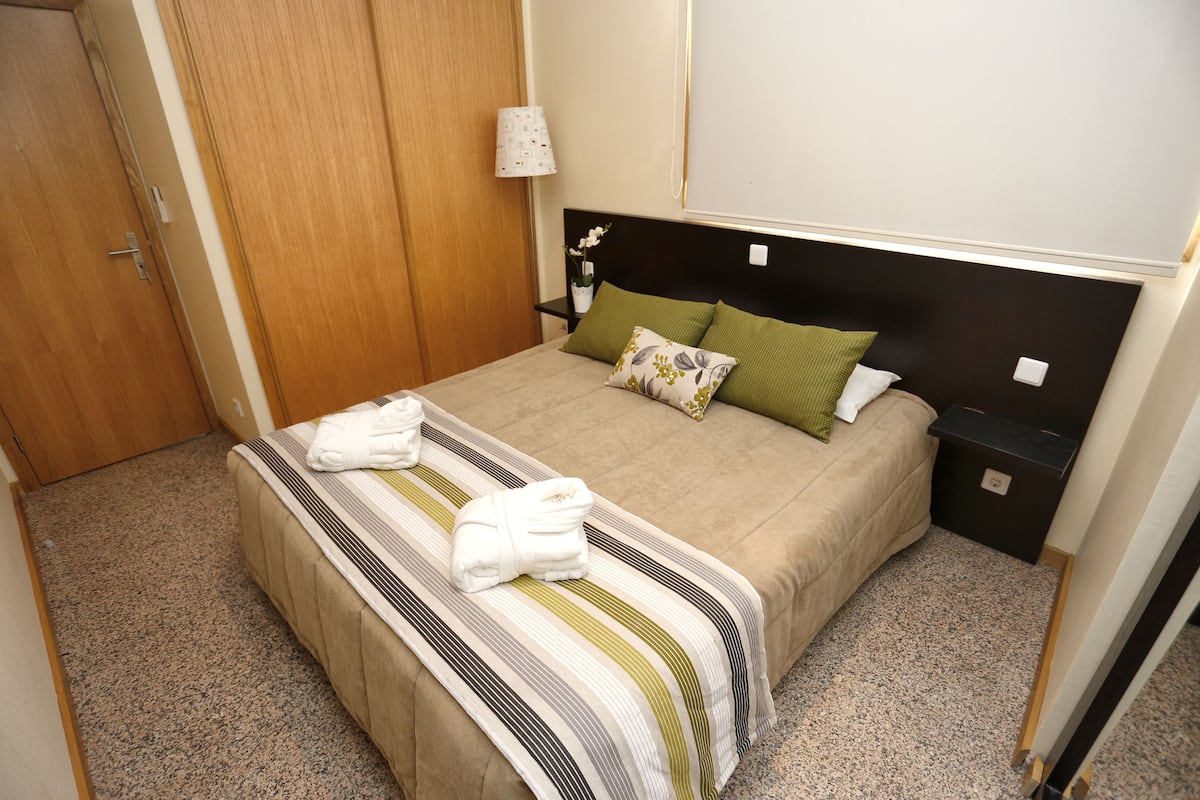 Un lit bien fait, avec une couvre-lit à rayures et deux oreillers, une table de chevet avec une lampe et une armoire en bois.