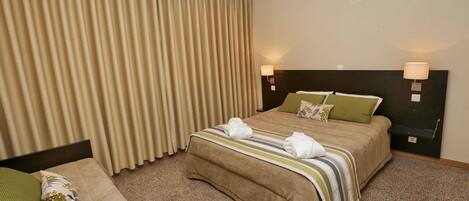A hotel room with a large bed, two bedside lamps, a headboard, and a window with curtains.