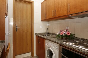 Una cocina compacta con armarios de madera, lavadora integrada, pileta de acero inoxidable y encimera de granito.